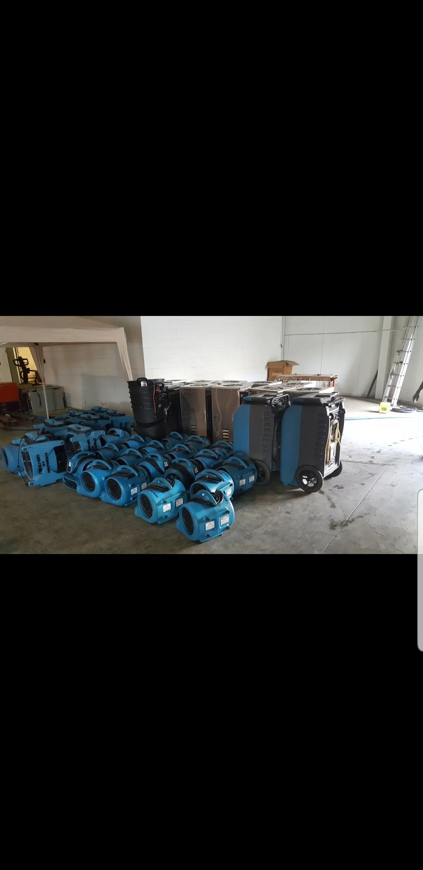 Blue air movers and gray dehumidifiers staged on concrete floor for water damage drying