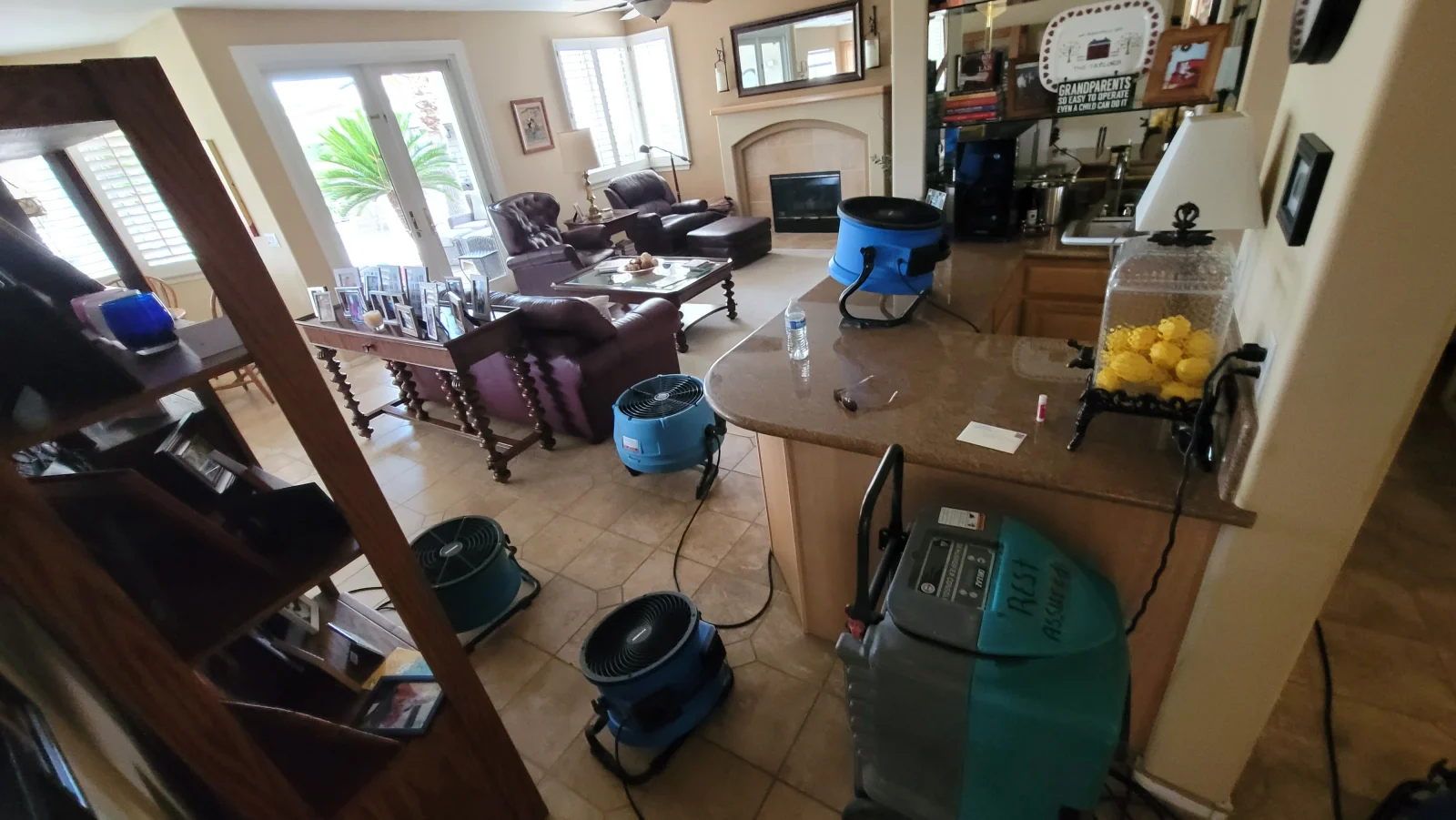 Blue air movers and a teal commercial dehumidifier drying tile floors in an open living room and kitchen