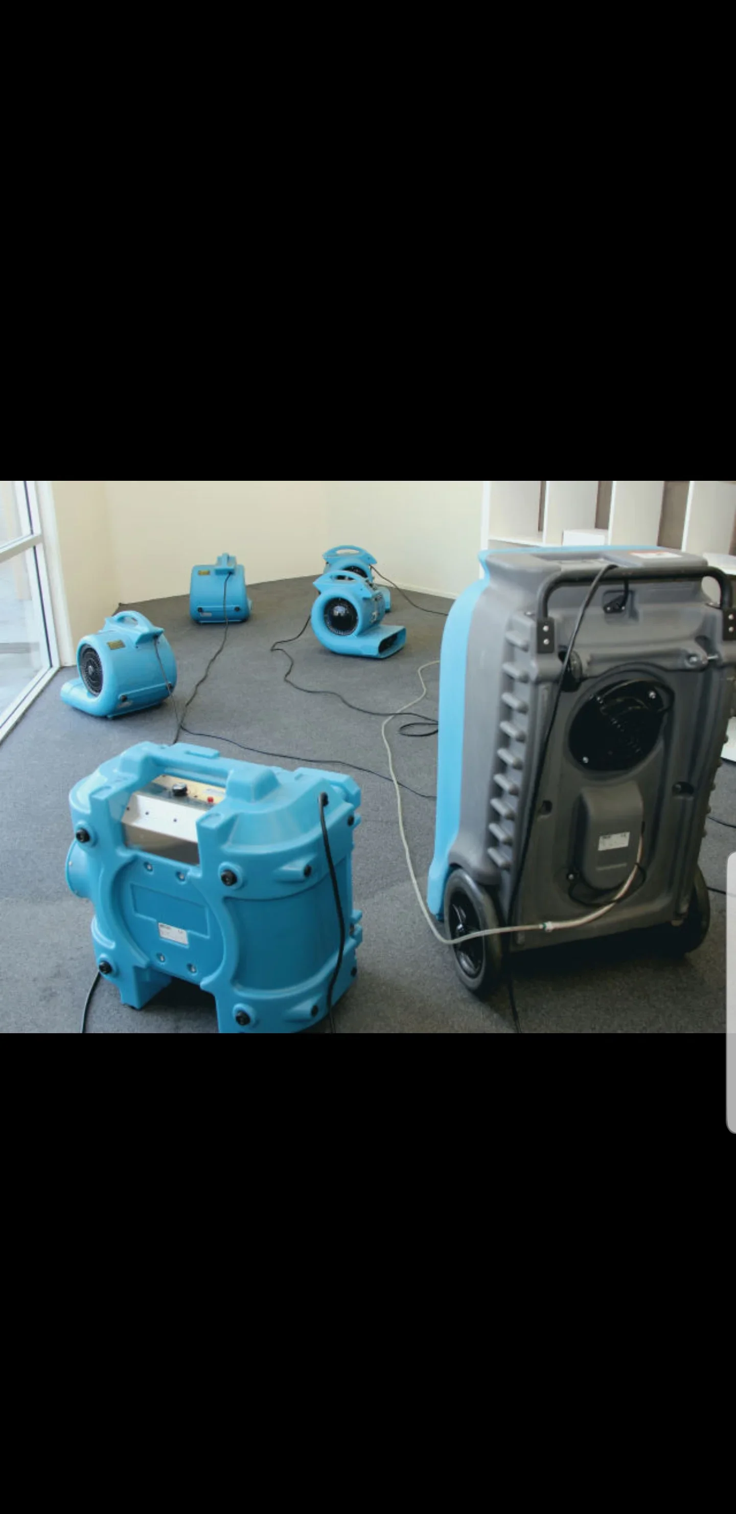 Blue air movers and gray dehumidifier drying a gray commercial carpet floor during water damage restoration