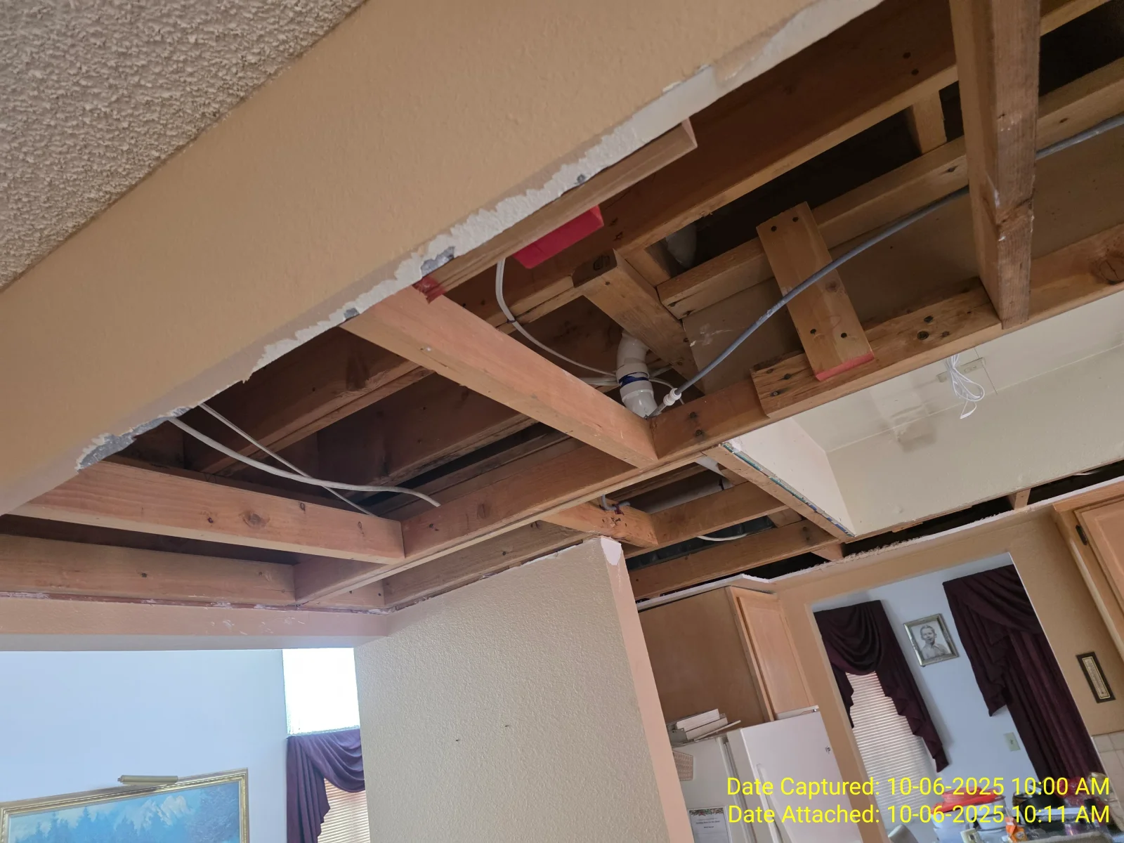 Exposed wood ceiling joists and blocking with white PVC drain pipe and electrical cable after drywall removal