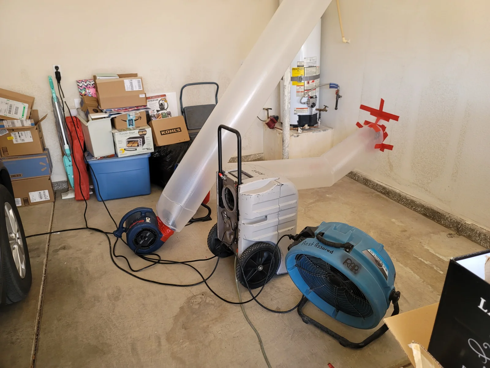 Garage drying setup with blue air movers, white dehumidifier, and clear flex ducting on concrete floor