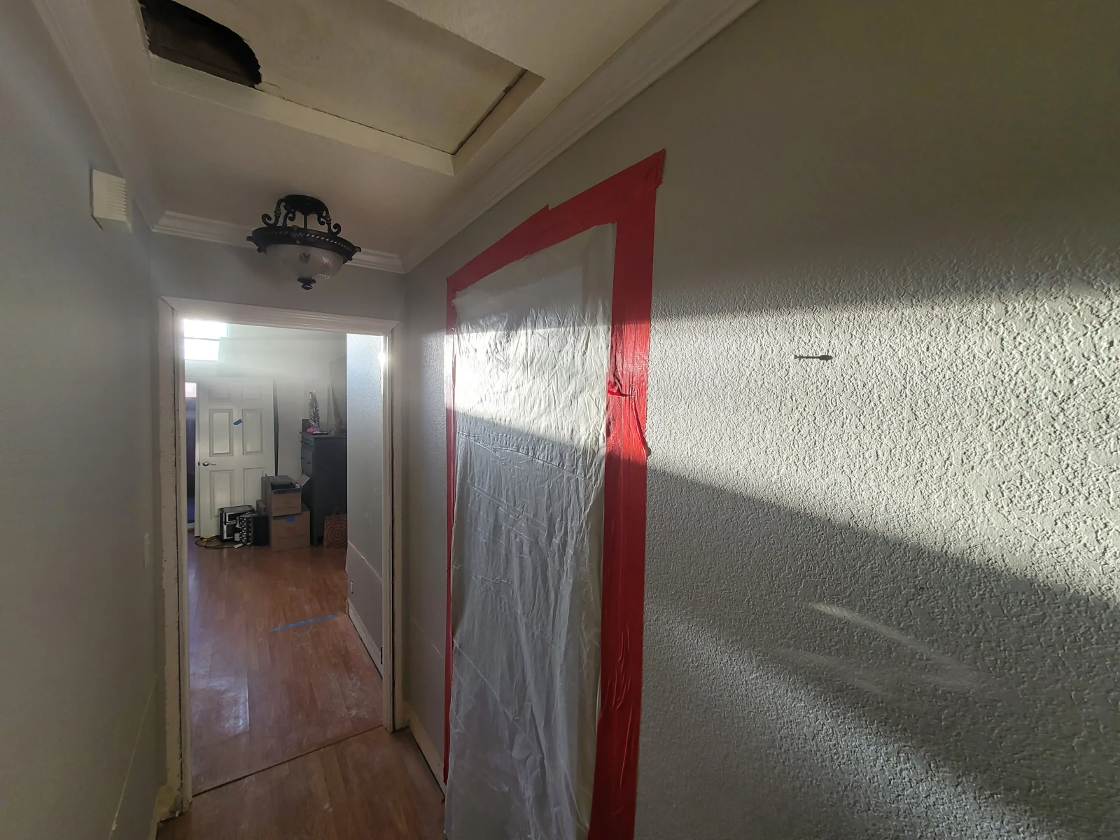 Hallway with textured walls, red tape and plastic sheeting masking a repair area, and a stained ceiling panel