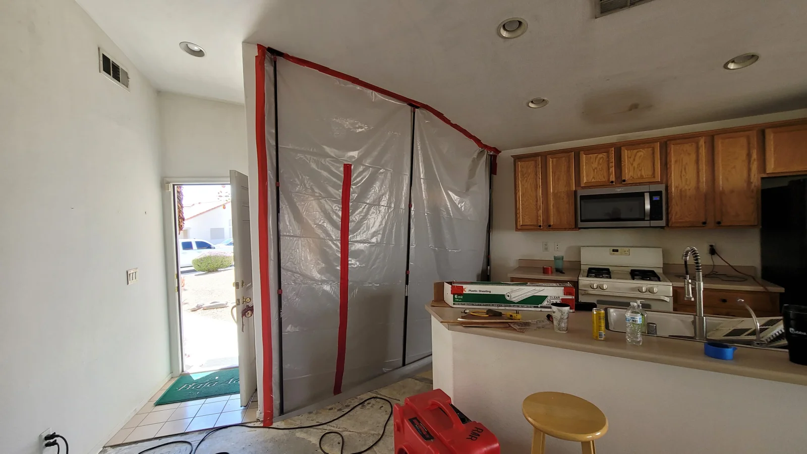 Clear plastic sheeting taped with red tape as containment barrier, red air mover, and tile floor in kitchen water damage work area